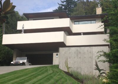 Modern house with a flat roof, multiple balconies, and an integrated carport, nestled on a landscaped hillside.