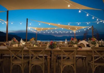 Outdoor event setup at twilight with string lights and floral centerpieces on dining tables.