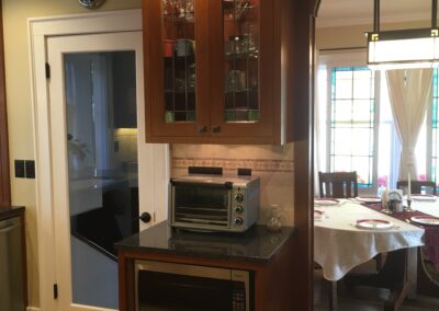 A kitchen corner featuring wooden cabinets, a microwave, toaster oven, and a dining area with a set table in the background.