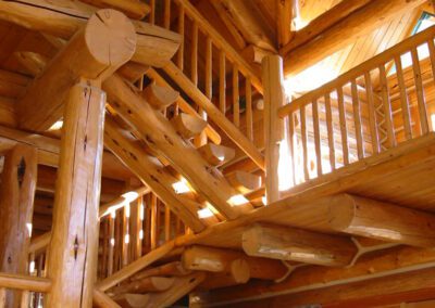 Wooden interior of a cabin featuring a log staircase and railings, with warm lighting.