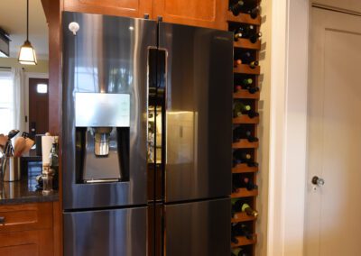 Stainless steel refrigerator with water dispenser integrated into wooden kitchen cabinetry beside a built-in wine rack.