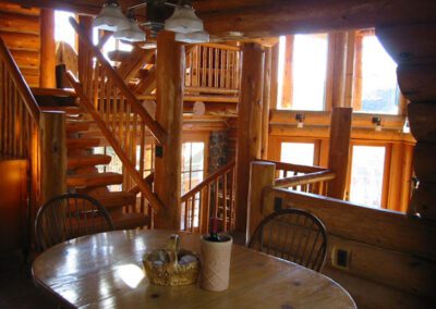 Interior of a wooden cabin with a spiral staircase and a round dining table near a window.