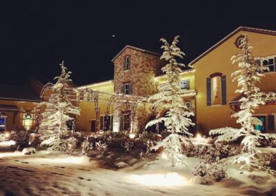 A serene winter night scene featuring snow-covered trees and a warmly lit building.