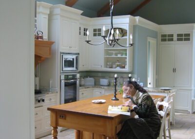 A person sitting at a wooden table reading in a bright kitchen with skylights and white cabinetry.