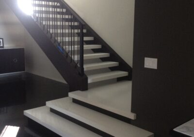 Modern staircase with white steps and black railings in a room with contrasting dark and light walls.