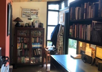 Cozy home office with wooden ceiling, bookshelf, and a desk, illuminated by natural light from a window.