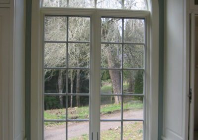 Arched window with a view of a park, situated above a white cabinet in a well-lit room.