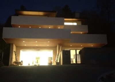 A modern multi-story house illuminated at dusk, with visible interior lighting and open garage.